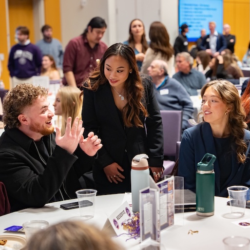 Students chat and network around a table at a busy campus event.
