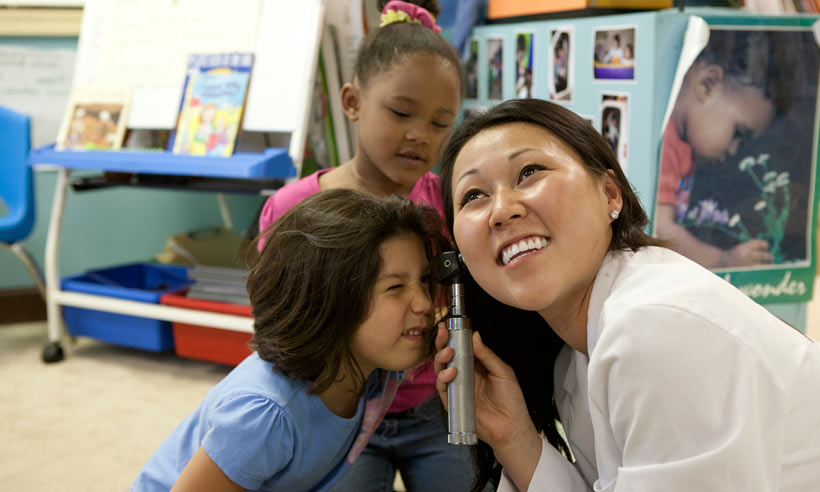 Curious children learn how to use an otoscope with the help of a JMU student in a white lab coat 