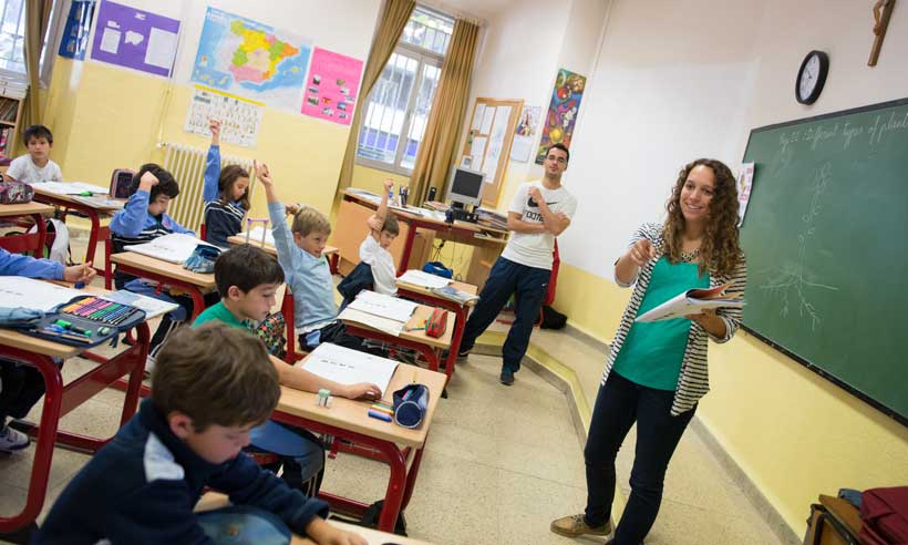Children in a classroom raising hands as student teacher calls for answer