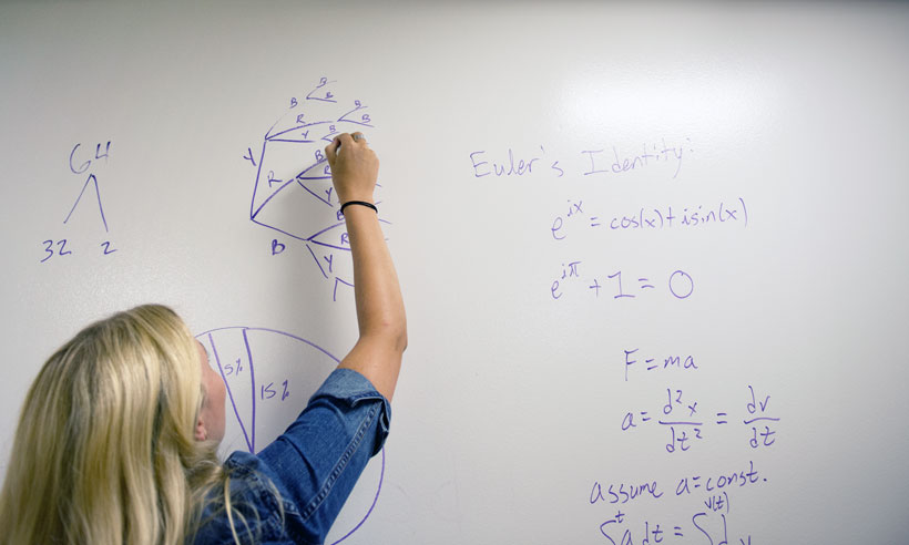 A JMU student solves a math problem at a white board