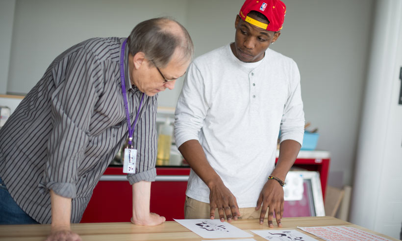 A student explains his artwork to a professor