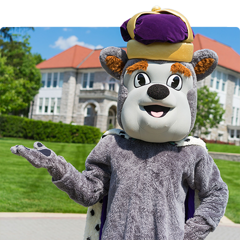 Duke Dog holding his hand out to the side with the Quad in the background.