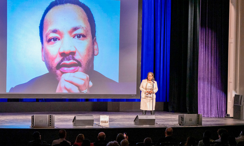 Presenter speaking to crowd in front of picture of MLK Jr.