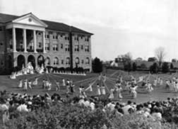A large crowd and the May Queen and her Court gather in front of Converse Hall to watch several simulaneous Maypole dances in 1936. 