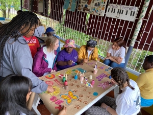 JMU students collaborate with a CUMI client on a piece of art. The paper banner includes images of butterflies, flowers, and rainbows, JMU logos, and Duke Dog footprints.