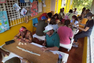 JMU students interact with CUMI clients. In the foreground, a group plays dominoes. In the middle ground, a group plays Jenga. In the background, a group plays cards.