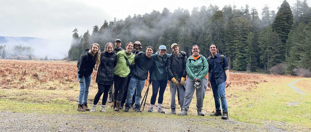 2023 ASB Redwood group pose in a meadow. In the background, fog partially obscures the trees