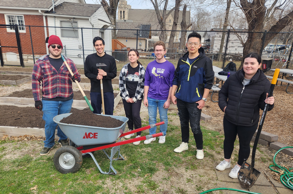 2023 ASB Sheffield group poses in the community garden with a wheelbarrow full of mulch