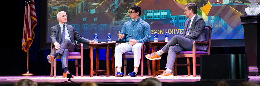 McFarlane sits on stage in Wilson Hall with Dr. Anthony Fauci and Jim Acosta for the Madison Vision Series panel on health issues like COVID-19.