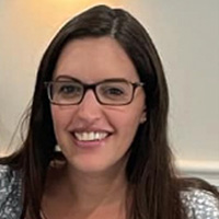 Smiling person with long dark hair and glasses, photographed indoors against a neutral background.