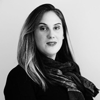 Black-and-white studio portrait of a woman with long hair wearing a scarf and a dark top, looking at the camera.