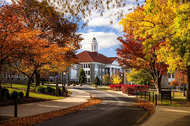A scenic view of JMU campus surrounded by vibrant autumn foliage, showcasing colorful trees and Wilson Hall in the background.