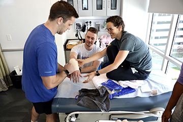 Three JMU students, two are putting a splint on a student's arem
