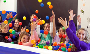 A group of smiling women in the JMU OTCES department enjoying a playful moment in a ball pit, surrounded by colorful balls.