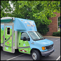 The Gus Bus with a whimsical design parked outside among trees.
