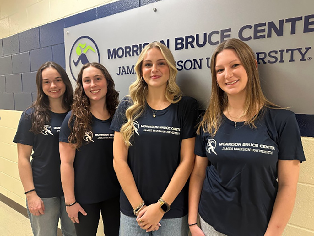 Four students in matching Morrison Bruce Center James Madison University T-shirts pose in a hallway in front of a Morrison Bruce Center sign.