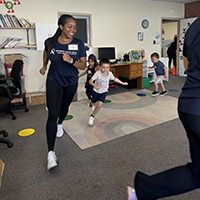 Children and an instructor running together in a classroom setting during a physical activity session.