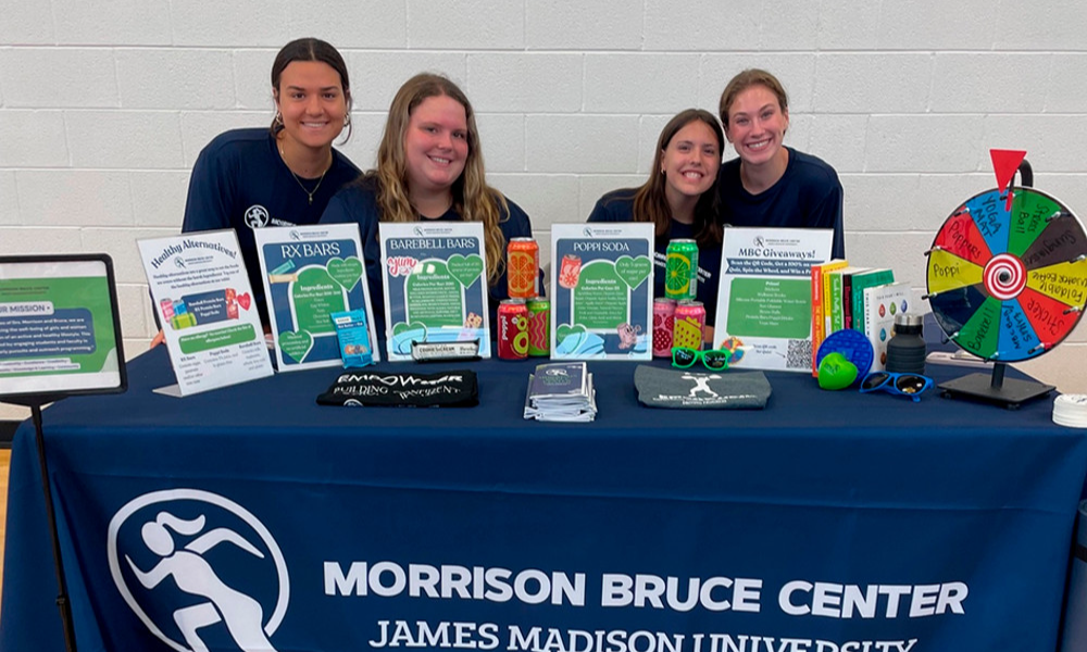 JMU students wearing Morrison Bruce Center shirts and setting at a table full of MBC flyers and merch