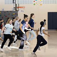 A fitness instructor guiding a participant on a treadmill in a gym setting, with various exercise equipment and other attendees in the background.
