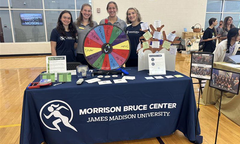 JMU students wearing Morrison Bruce Center shirts and setting at a table full of MBC flyers and merch