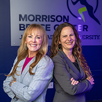 Photo of Dr. Cathy McKay and Dr. Jill Lassiter, smiling and standing back-to-back, showcasing the Morrison Bridge Center logo in the background.