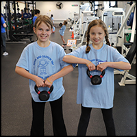 Movin' and Groovin' Day - Two girls in matching blue t-shirts are smiling while holding kettlebells in a gym setting.