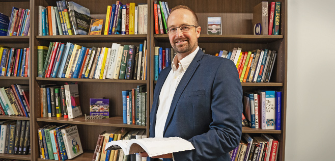 Adam Vanhove stands in front of book shelf