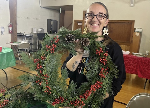 woman smiling and holding holiday wreath up that she made