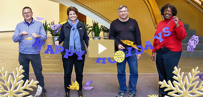 four people standing with a happy holidays sign