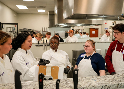 Valley Scholars students in white chef coats and aprons work together at a kitchen workstation during a class.