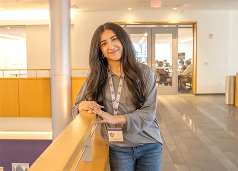 Sana Jaf leaning on a railing in Hartman Hall with a conference room in the background.