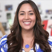 A headshot of Claudia Robles Arias wearing a blue and white blouse, smiling