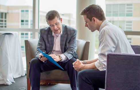 A man sits with a student looking over a resume.