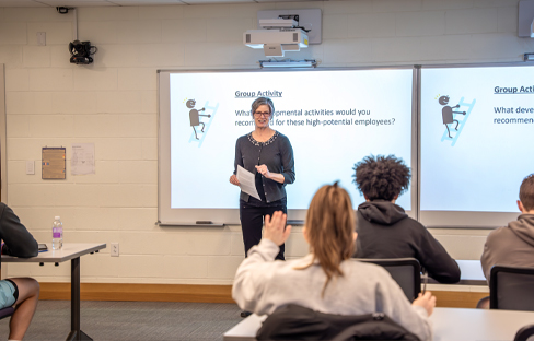 A professor teaches in the front of a stadium-style classroom. Students sit at desks.