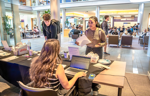Two students lean over the employer table in the Hartman Hall atrium.