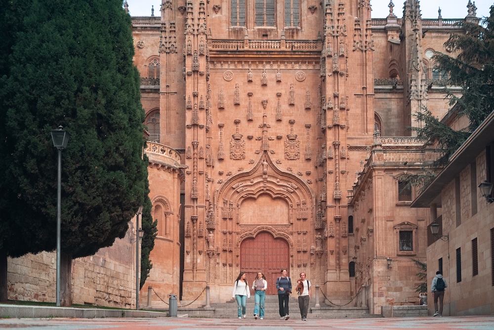 A group of four people walking in front of an ornate, historic building with intricate architectural details.
