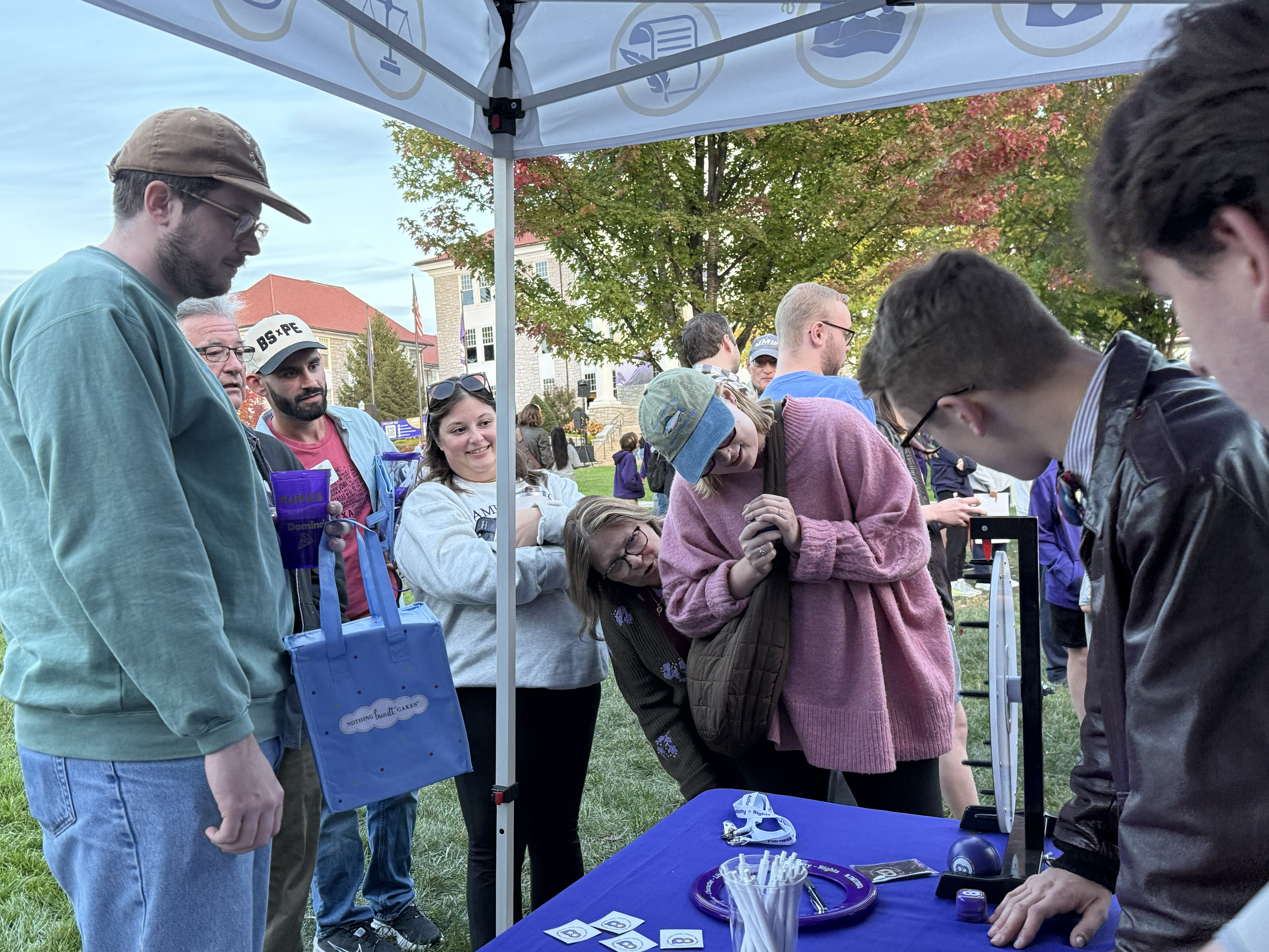 A lively outdoor event with a group of people gathered around a table, engaging with a vendor and exploring promotional materials.