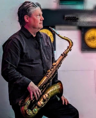 man leaning against the wall holding a saxophone