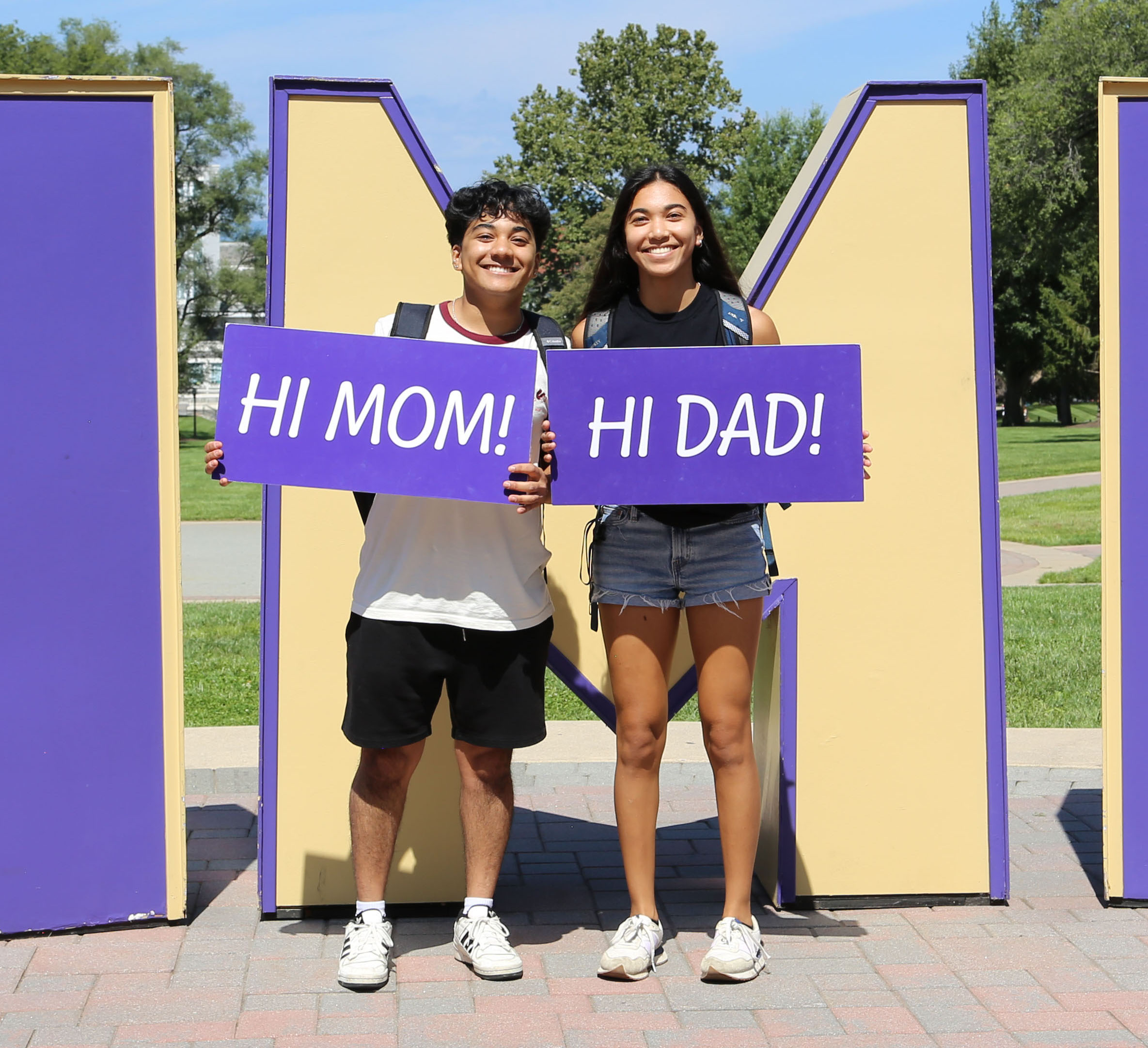 Students holding signs 'hi mom' and 'hi dad'