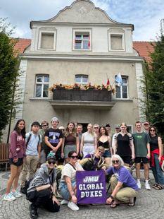 A group of students and faculty smiling and holding JMU Global Dukes Sign