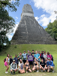 A group of students standing in front of a pyramid smile for a photo