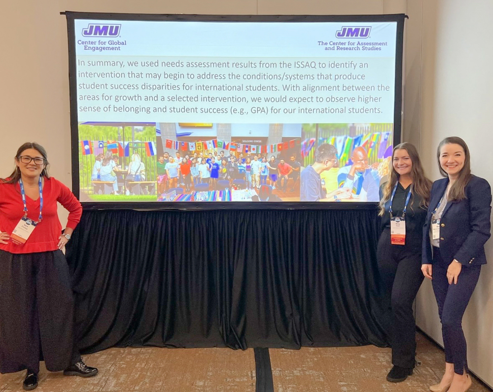 Marlee smiles for a photo in front of presentation with two colleagues