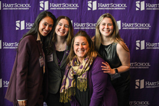 Four women smiling and posing together in front of a Hart School step-and-repeat banner.