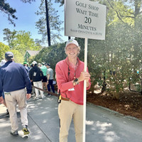 A male Hart School student holding a sign indicating a 20-minute wait time for the golf shop at a sporting event.