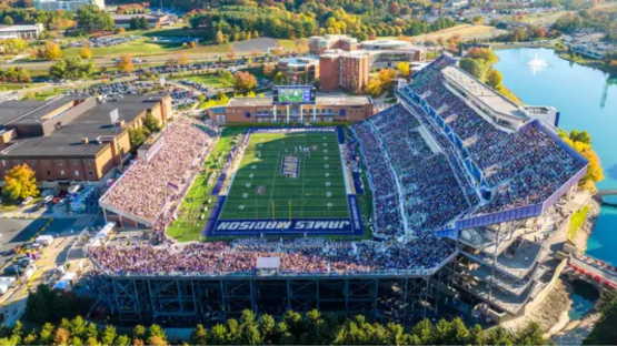 Aerial view of a packed football stadium with a green field and grandstands beside a river.
