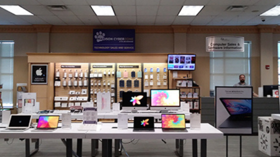Electronics store display with laptops and tablets on tables and a wall of phone accessories behind them.