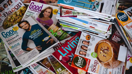 Stack of food and lifestyle magazines scattered on a table, with colorful covers and recipe headlines.