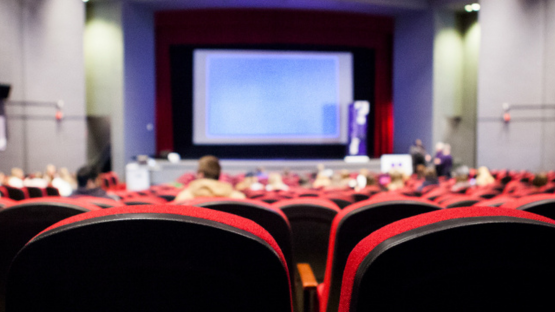 Rows of red theater seats facing a large presentation screen in an auditorium.