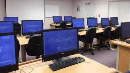 Computer training classroom with rows of desktop monitors and chairs on long desks.