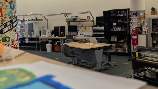 Makerspace workshop with tables, chairs, equipment, and shelves of tools and supplies.